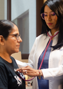 Mujer profesional de la medicina utilizando un estetoscopio en una paciente para examinar su corazón.