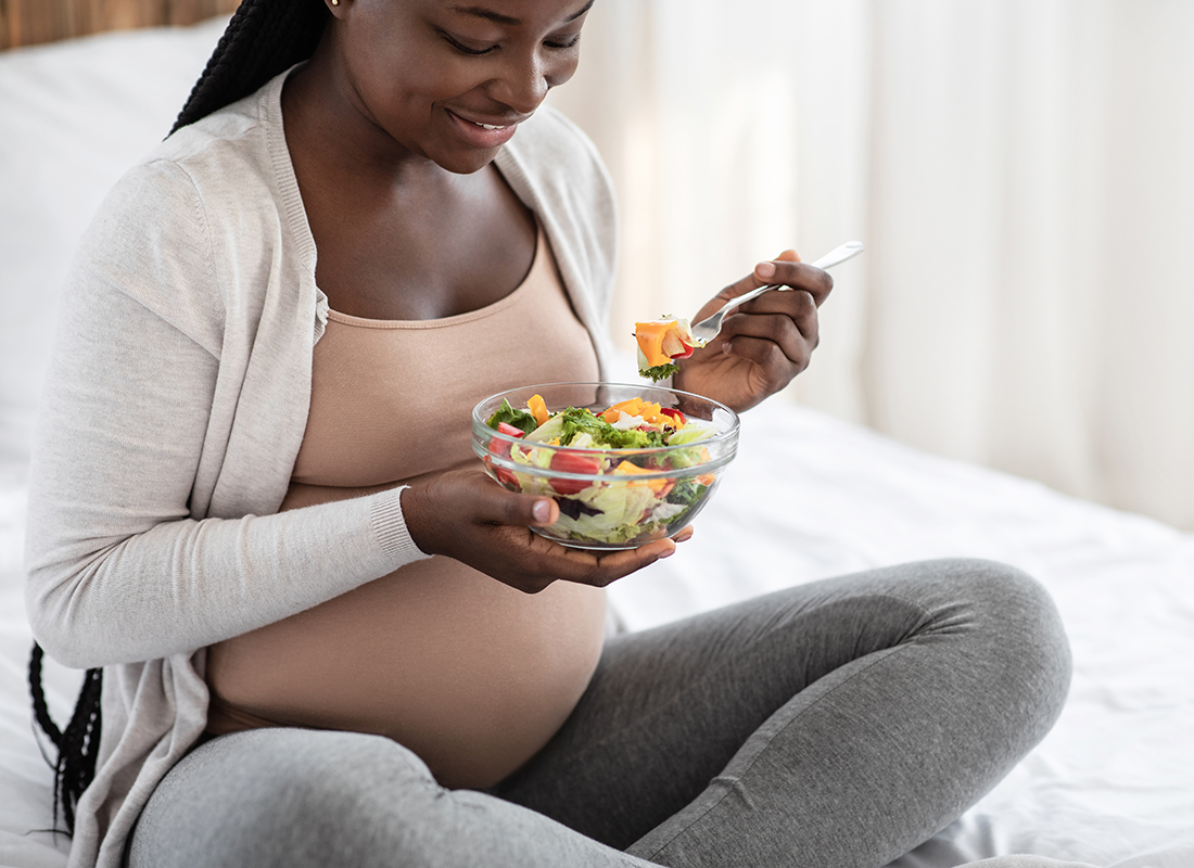 Mujer embarazada de origen africano comiendo una ensalada