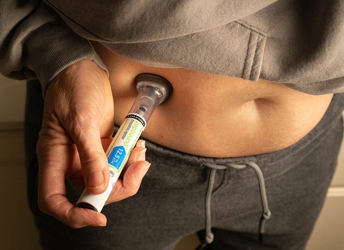 Woman using an injector pen to administer GLP-1 into abdomen.